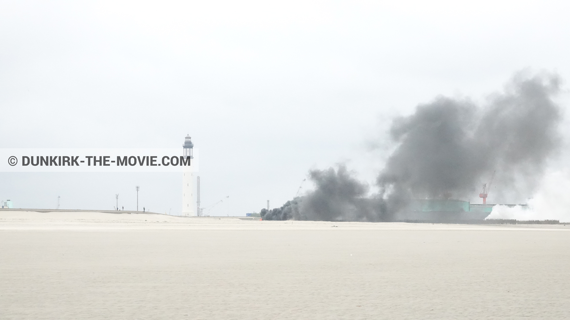 Photo avec ciel gris, fumée noire, phare de Dunkerque, plage,  des dessous du Film Dunkerque de Nolan