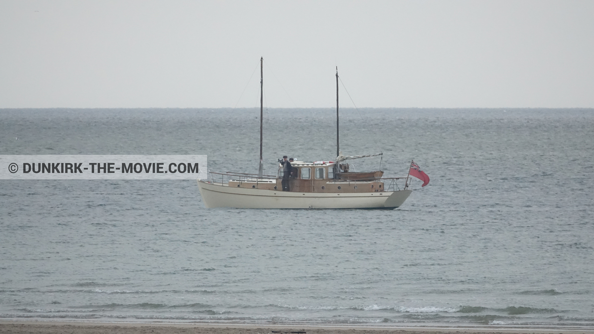 Picture with beach, grey sky, calm sea, supernumeraries, boat,  from behind the scene of the Dunkirk movie by Nolan