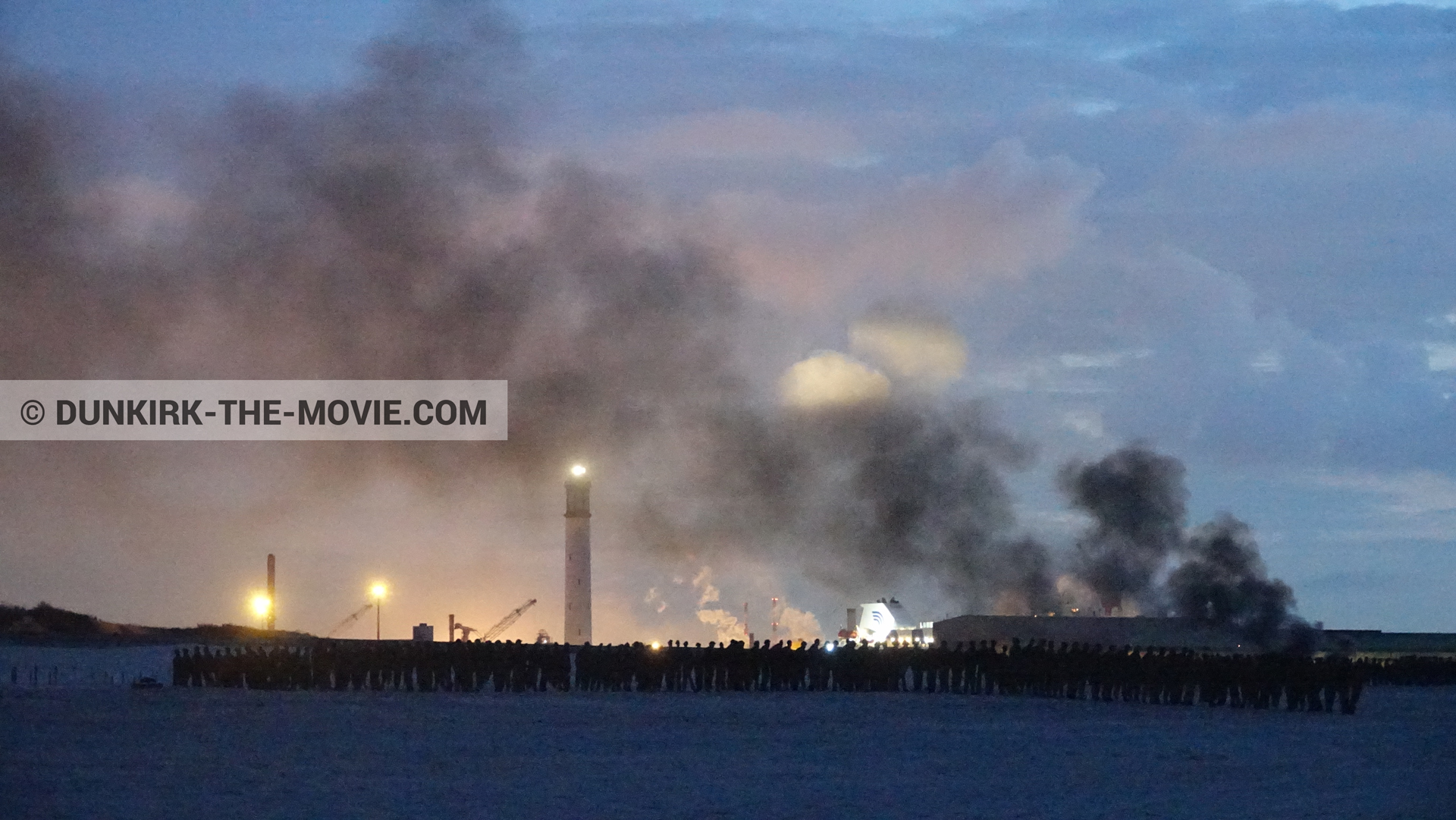 Photo avec ciel bleu, ciel orangé, fumée noire, phare de Dunkerque, plage,  des dessous du Film Dunkerque de Nolan
