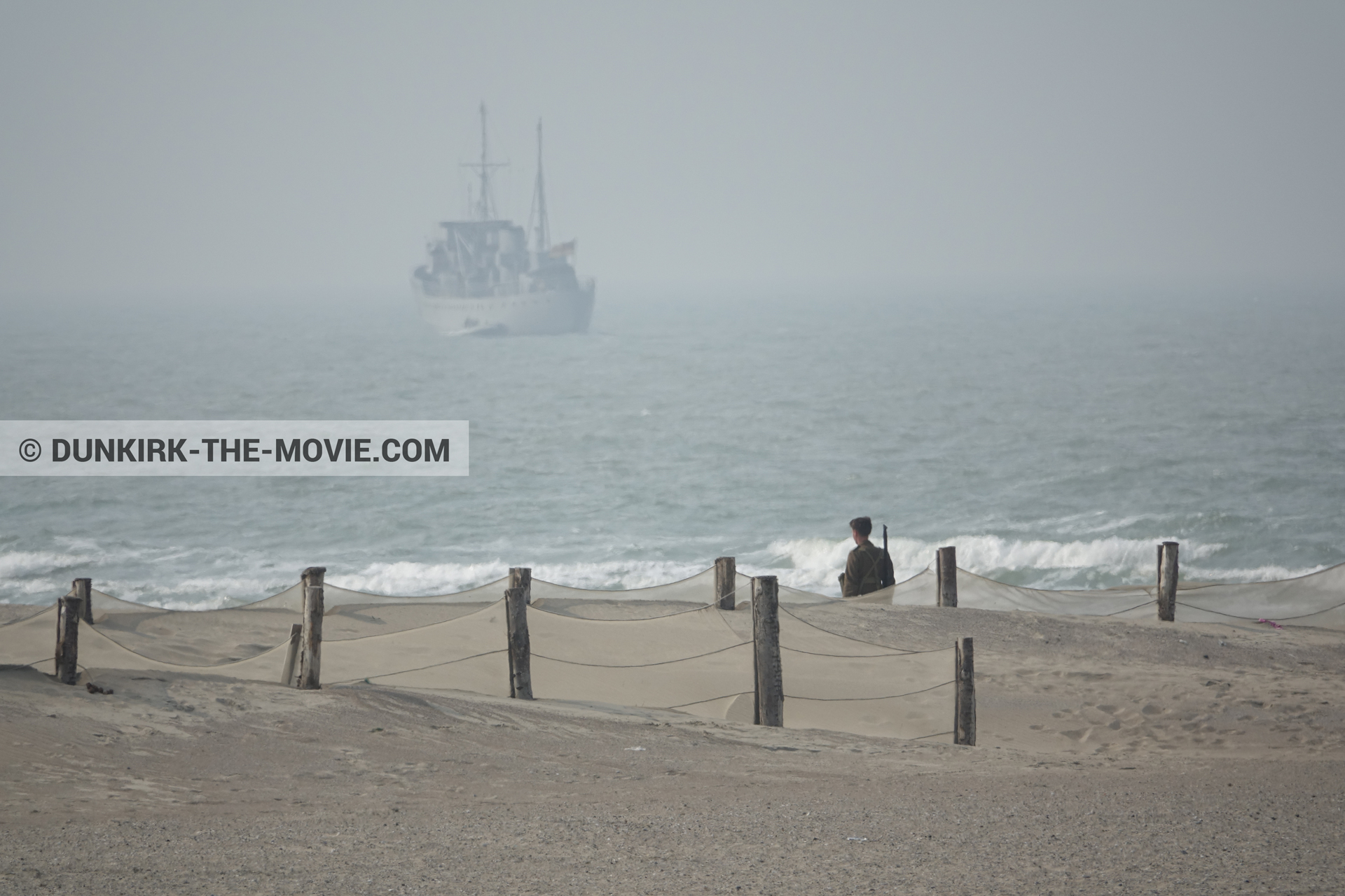 Picture with boat, grey sky, supernumeraries, rough sea, beach,  from behind the scene of the Dunkirk movie by Nolan