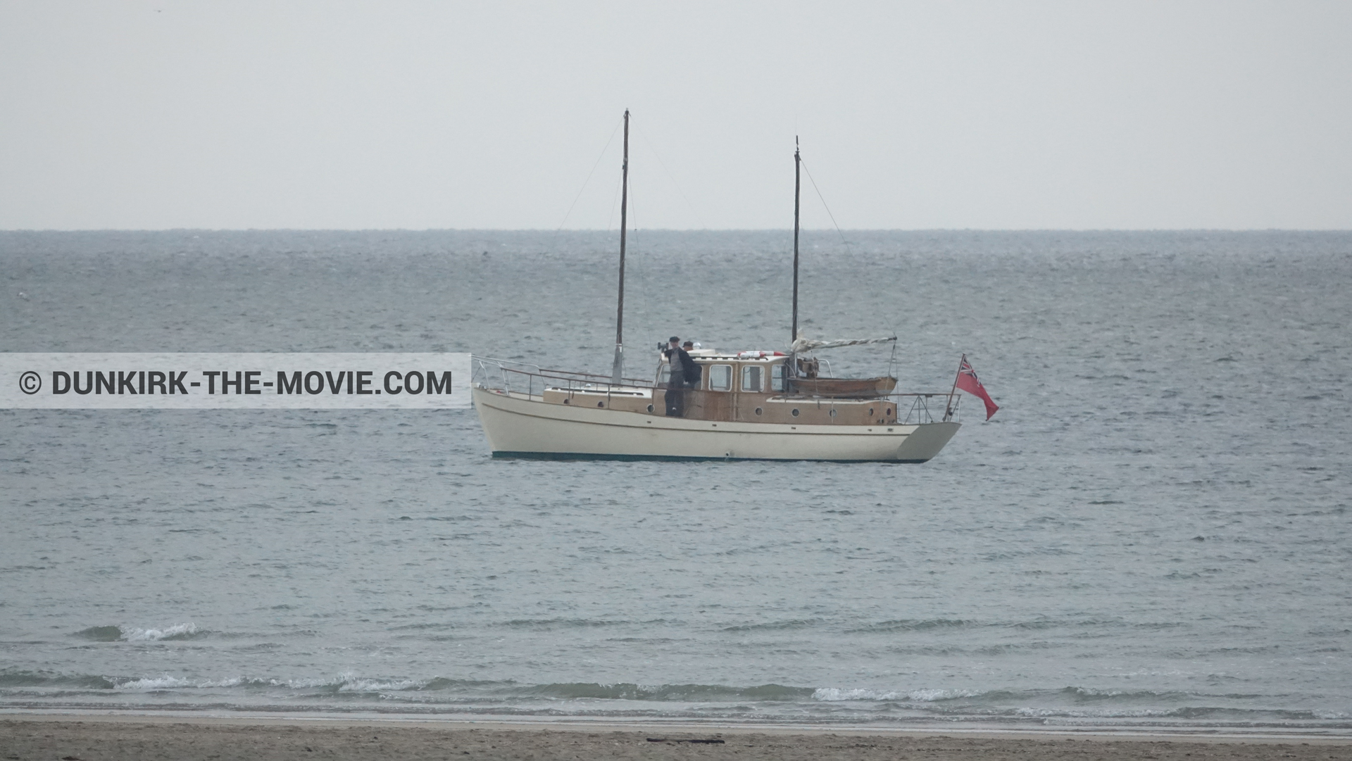 Picture with beach, calm sea, supernumeraries, grey sky, boat,  from behind the scene of the Dunkirk movie by Nolan
